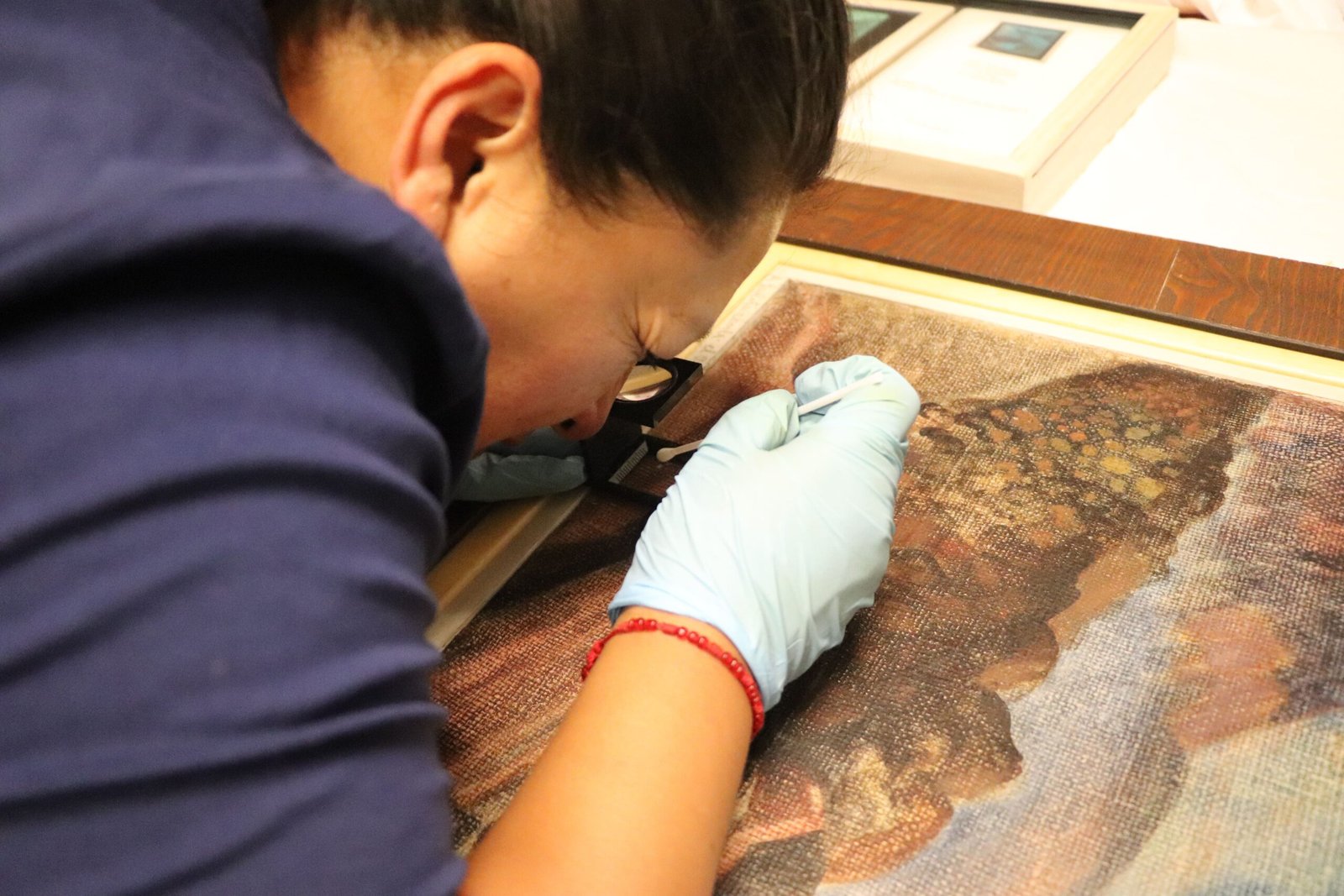 Mujer con una lupa revisando una obra pictórica.