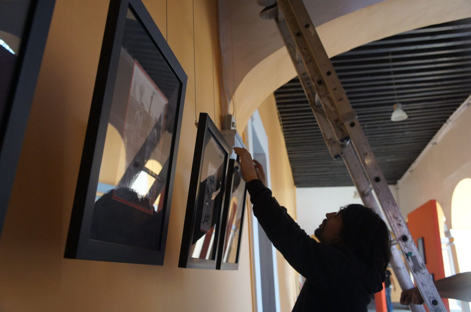 Persona montando unos cuadros, junto a una escalera.