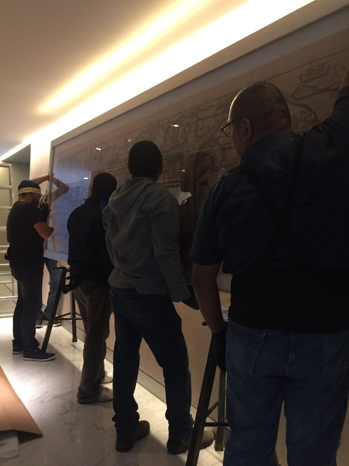 Personas colocando un cuadro grande en una pared.